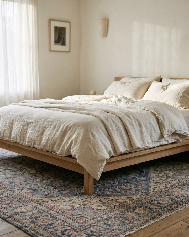 Hand-knotted Afghan rug in faded indigo under an oak bed with linen bedding