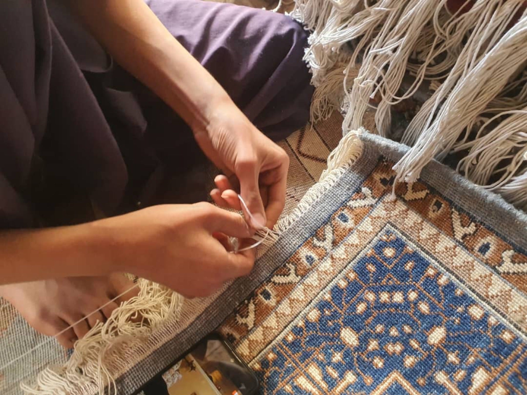A weaver's hands knotting the fringe of a hand-woven rug
